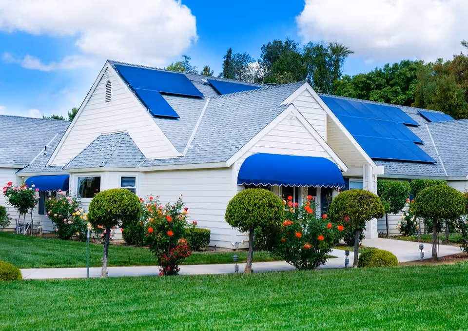 White senior living building with blue awnings, solar panels, and landscaped lawn.