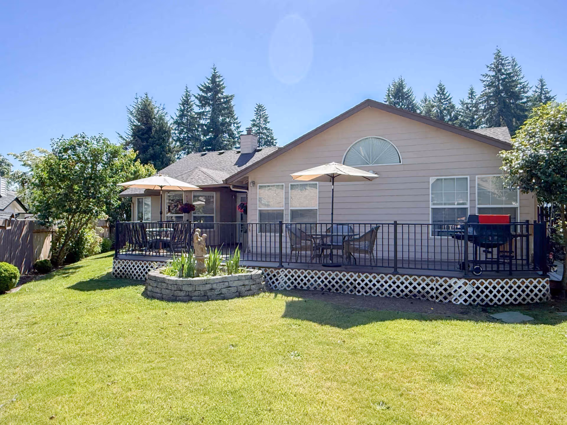 A single-story residence with a raised deck, patio furniture, umbrellas, and a grassy yard.