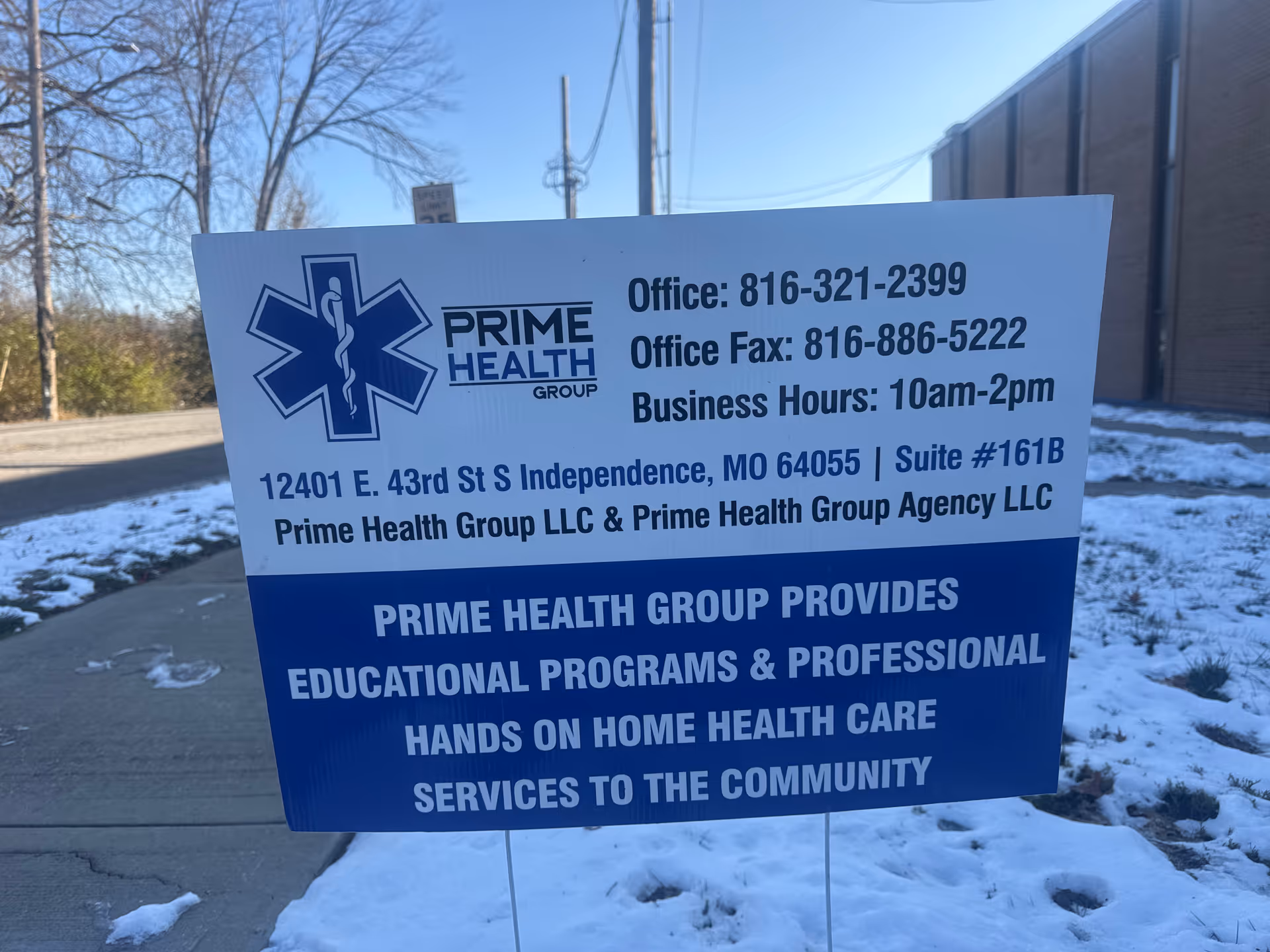 Outdoor sign for Prime Health Group LLC on a snowy sidewalk beside a building.