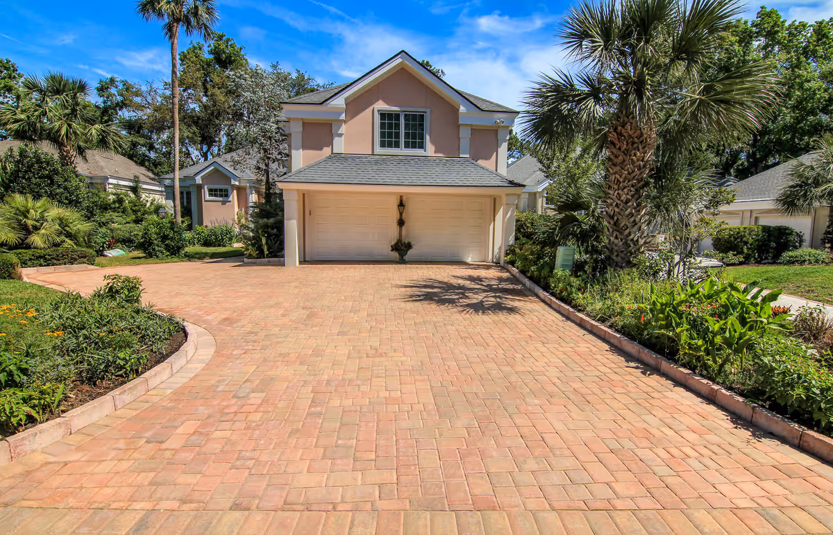 Front view of a pink two-story house with a brick driveway and landscaped yard.