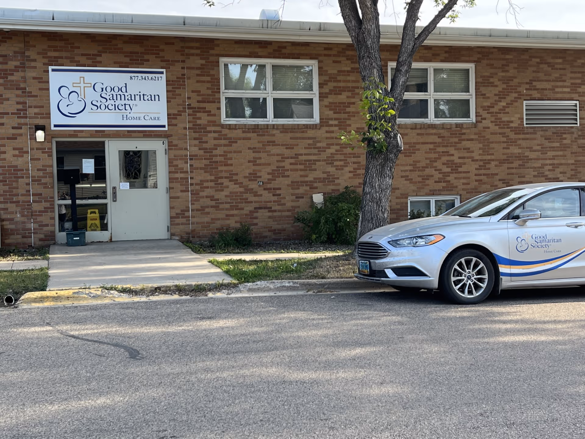 Brick building with Good Samaritan Society sign, entrance door, and parked car.