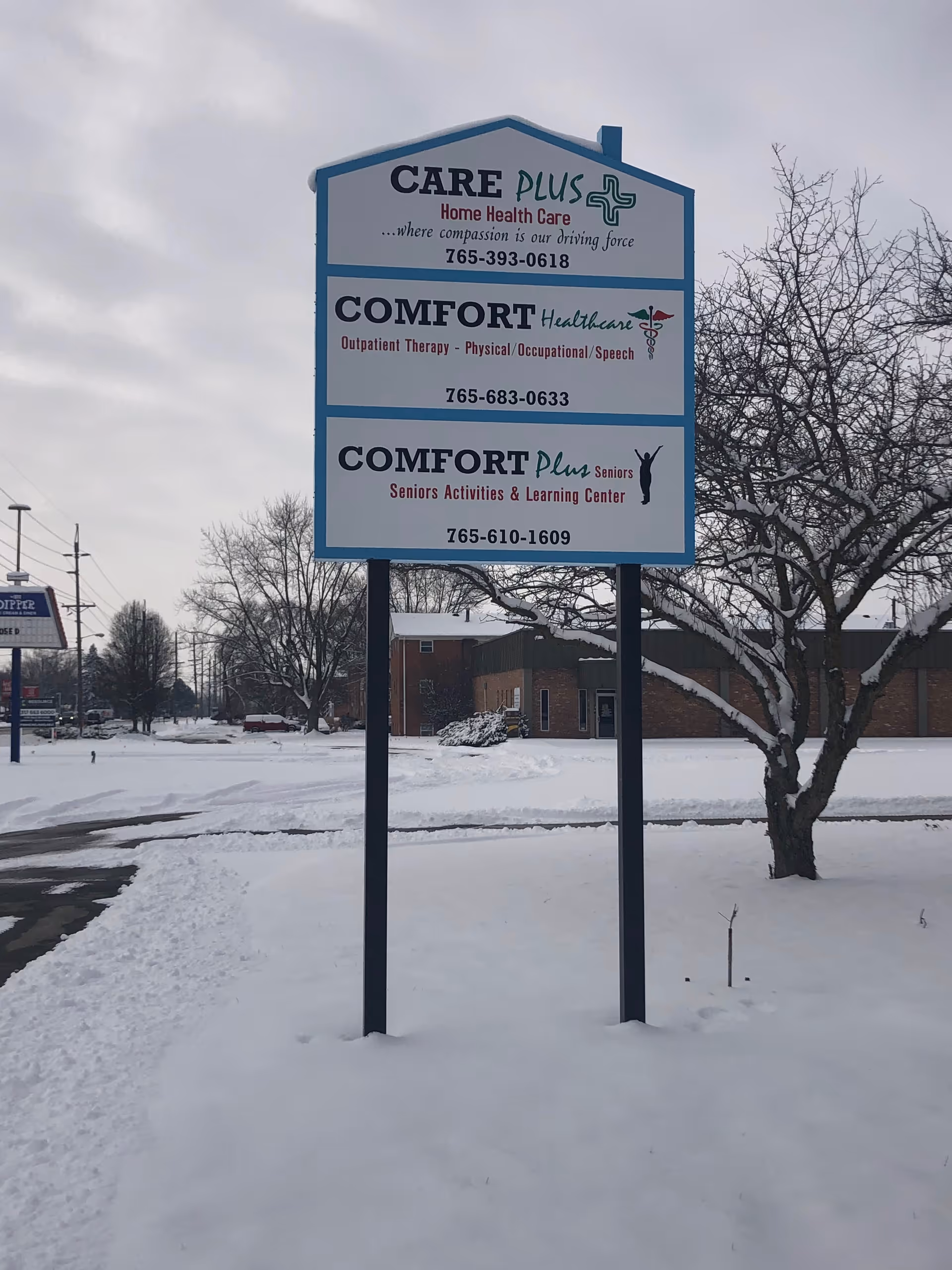 A large outdoor sign for Care Plus and Comfort Healthcare on a snowy lawn.