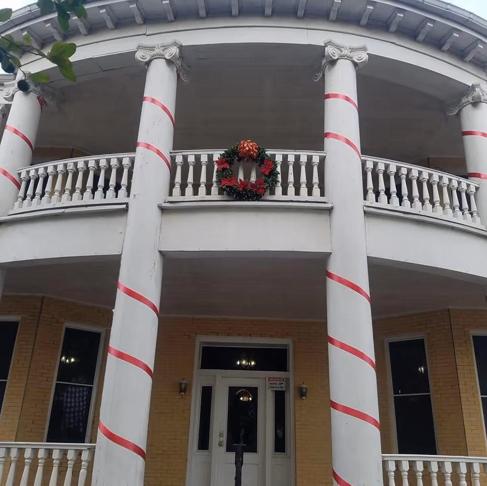 Front of a building with striped columns and a wreath on the balcony.