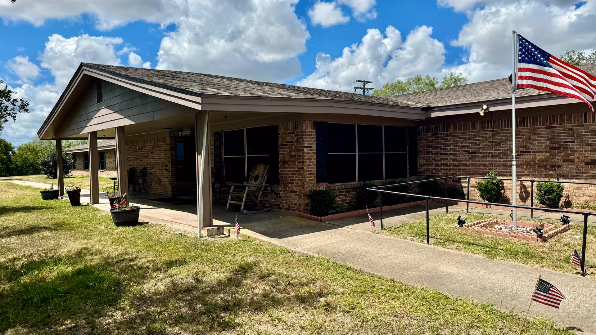 Single-story brick senior living facility exterior with a covered entrance and flags.