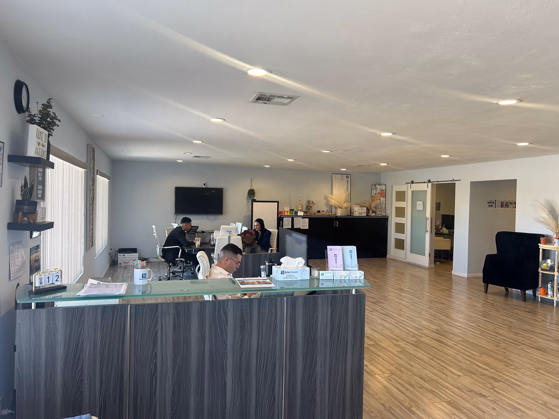 Bright open reception lobby with a dark wood front desk, staff at desks, and seating.