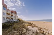 Coastal senior living building with balconies beside a sandy beach and ocean.