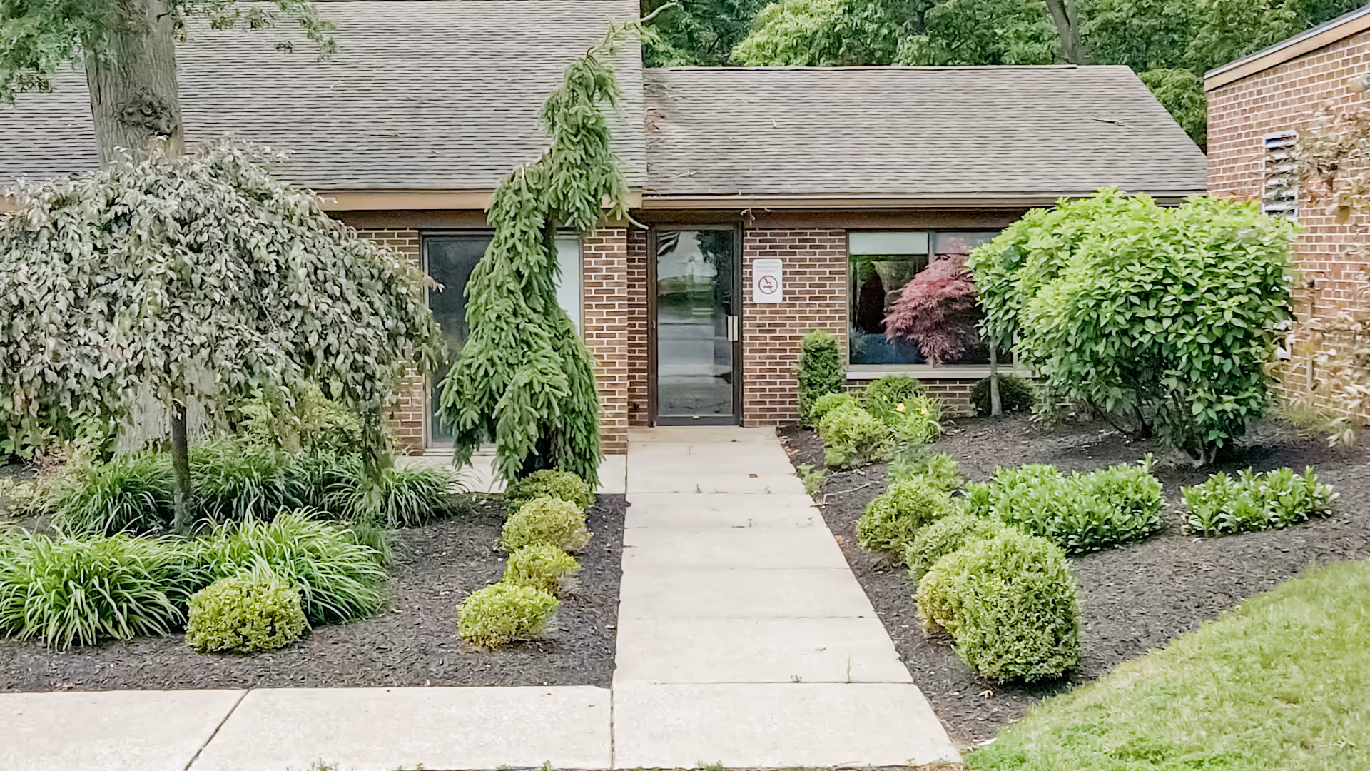 Aperion Care Demotte entrance with brick exterior, walkway, and landscaped shrubs.