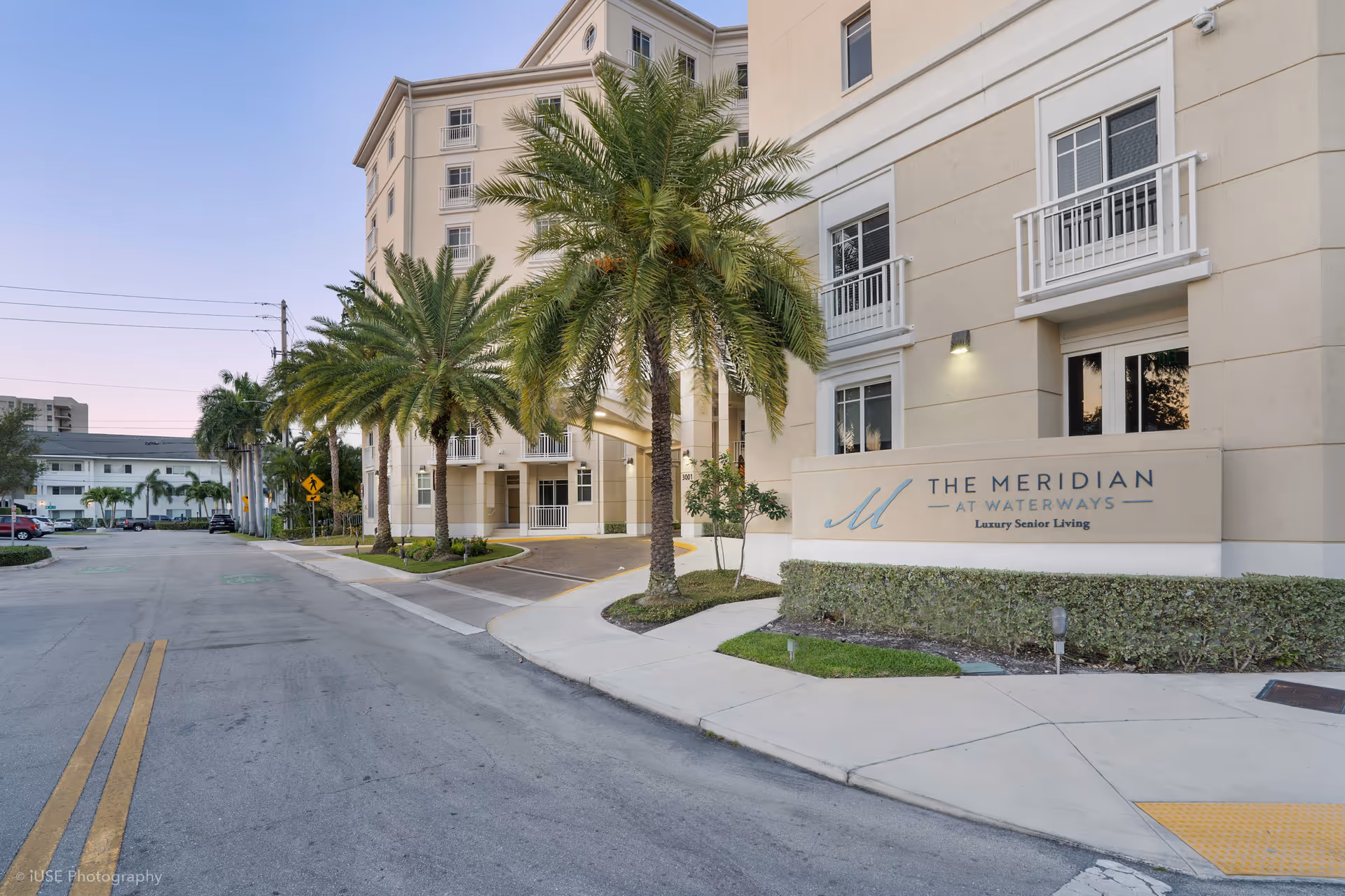 Exterior view of The Meridian at Waterways, a beige senior living building with palm trees.
