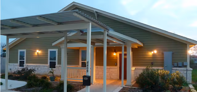 Single-story senior living facility exterior with a covered entrance, porch, and landscaped front yard.