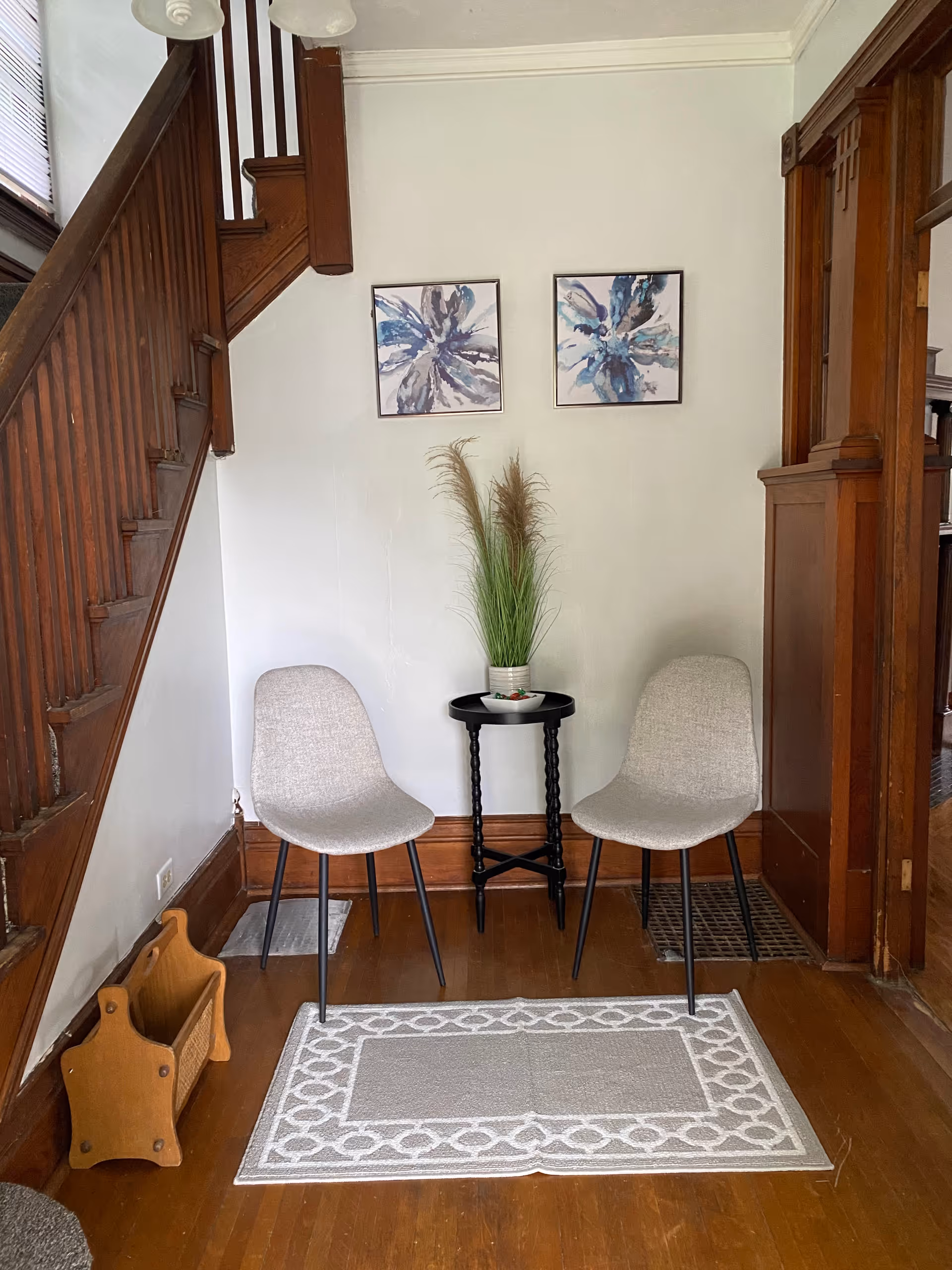 Two gray chairs flank a small round table with a potted plant near stairs.