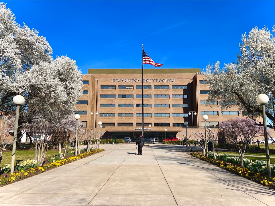 Howard University Hospital building with flag, walkway, and flowering trees along the entrance path.