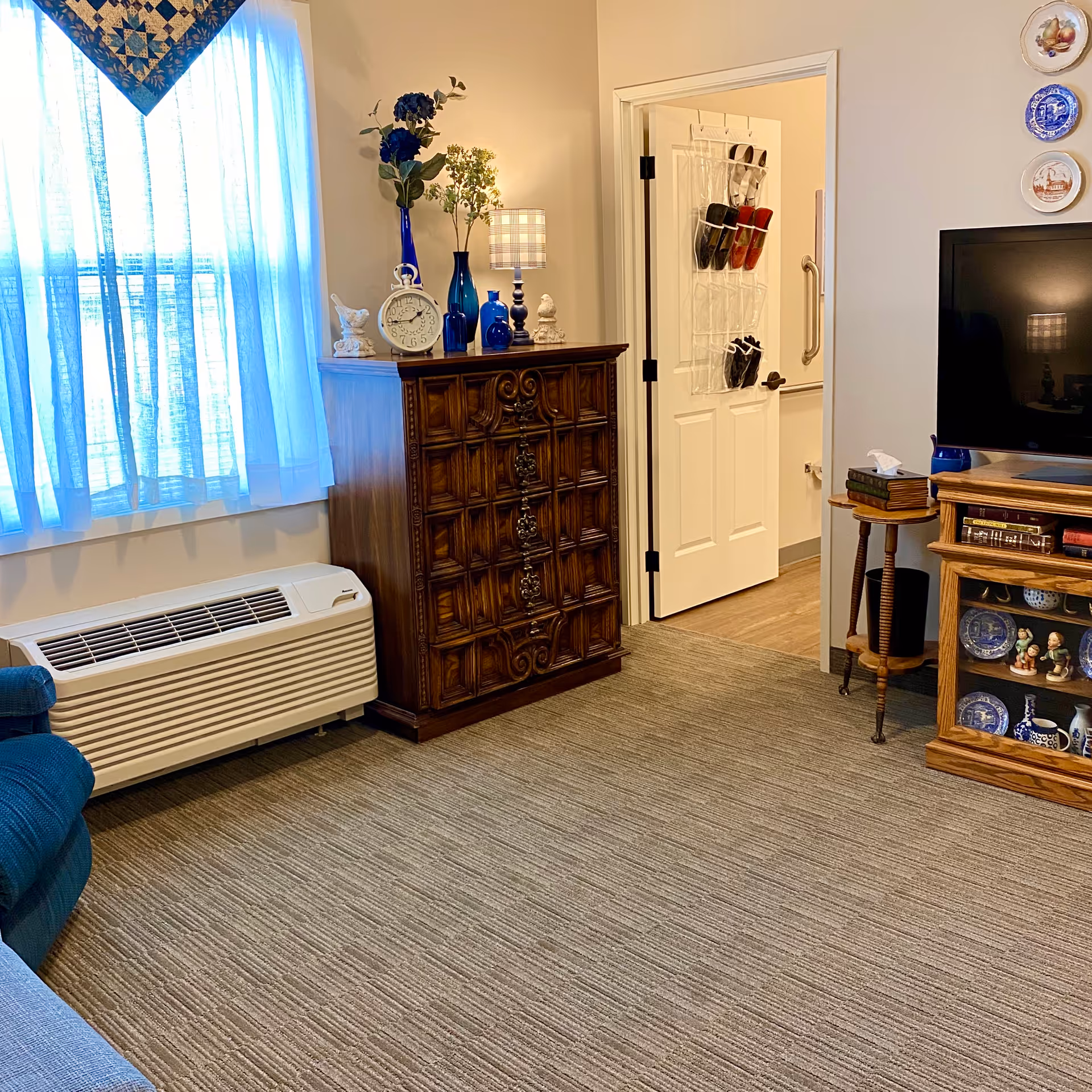 Cozy living room with blue accents, wooden dresser, TV, and doorway.