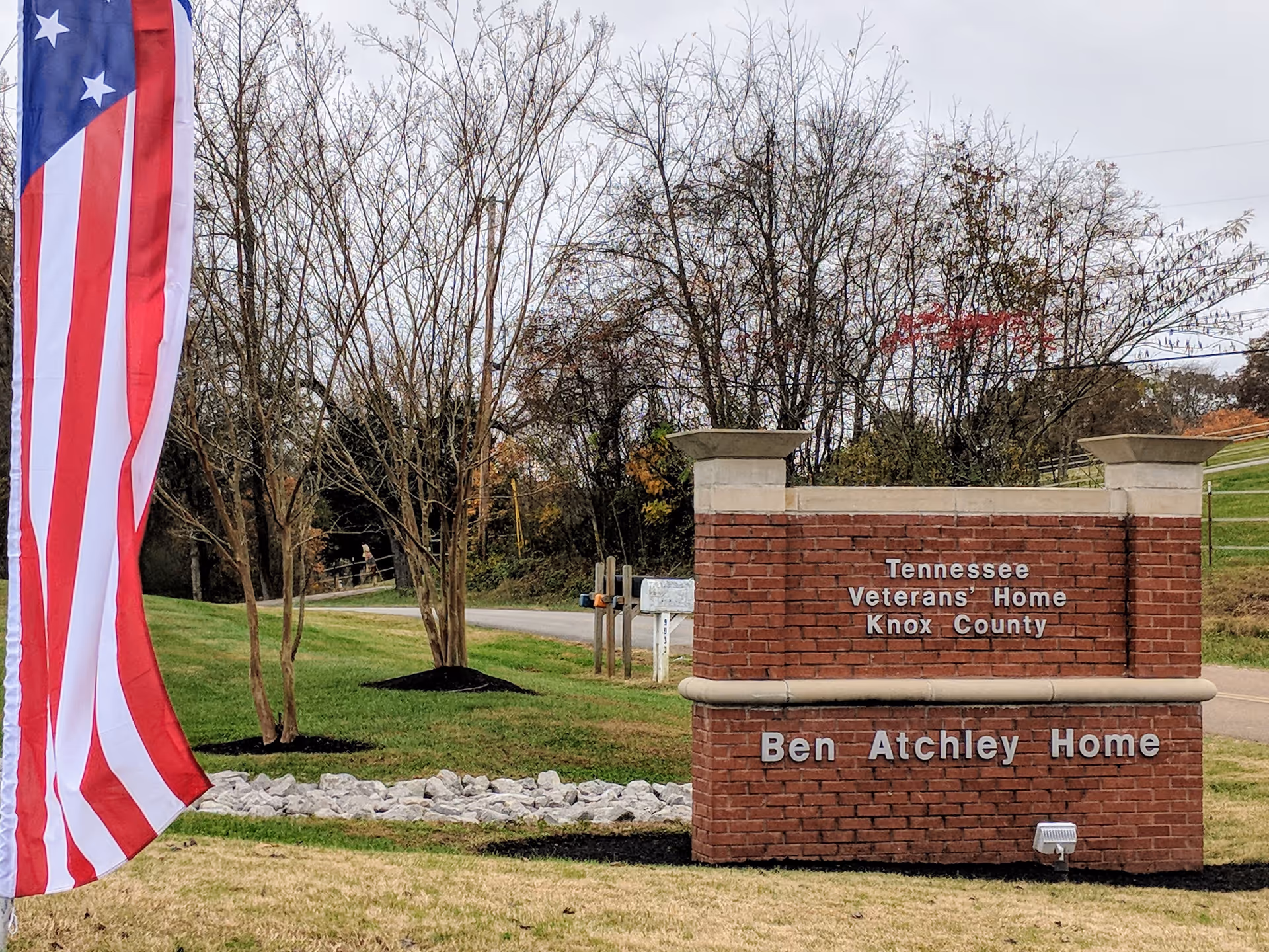 Red brick entrance sign reads Ben Atchley Home at Tennessee State Veterans' Homes beside flag.