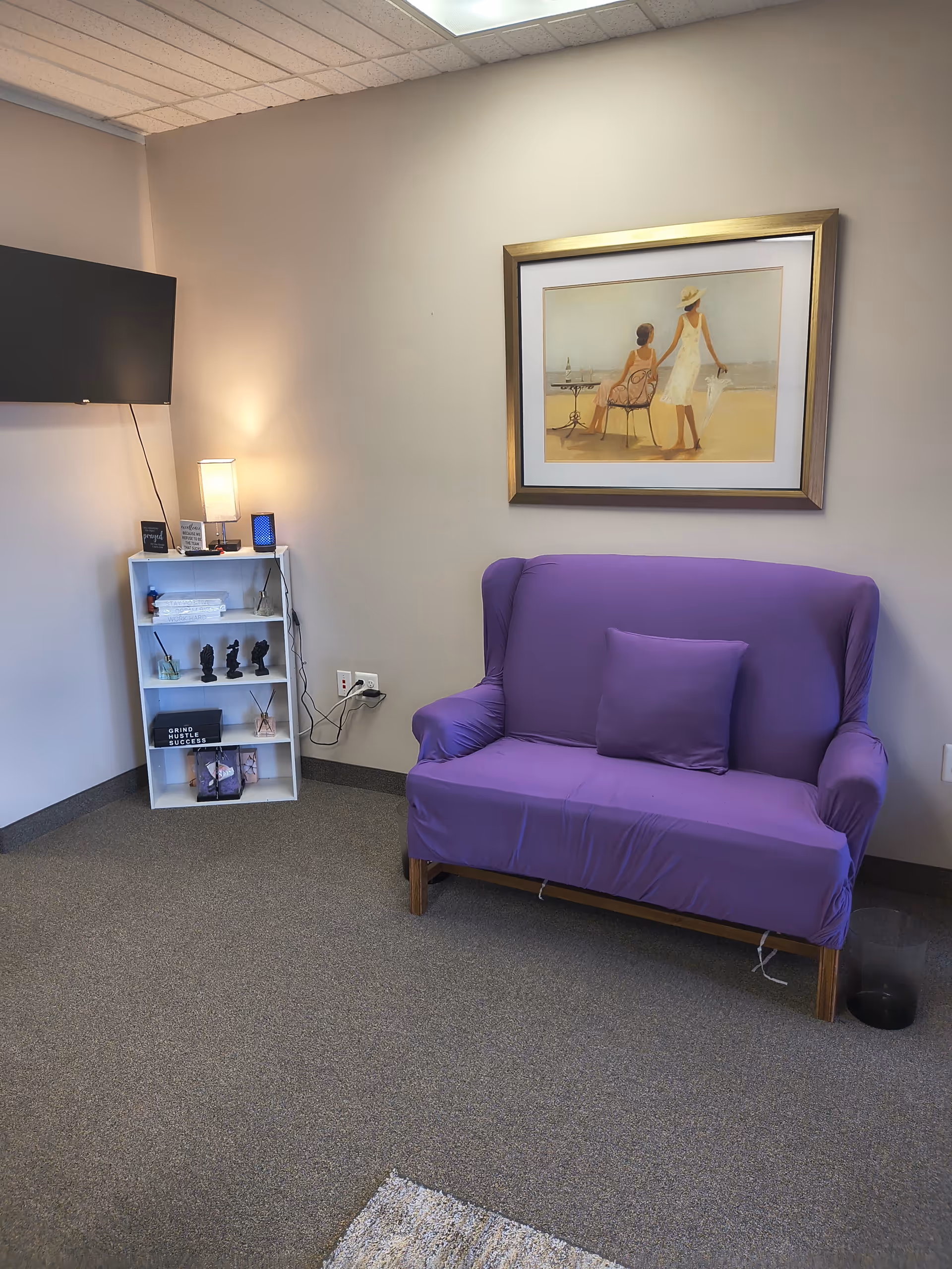 Purple sofa in a small, well-lit lounge with a painting and TV.