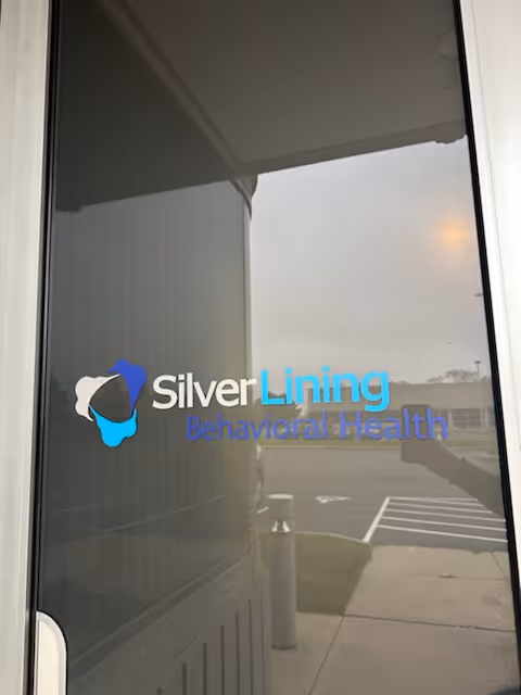 Glass entrance door with Silver Lining Behavioral Health logo reflecting the parking lot outside