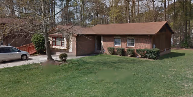 A single-story brick building with a driveway, car, and a well-kept front lawn.