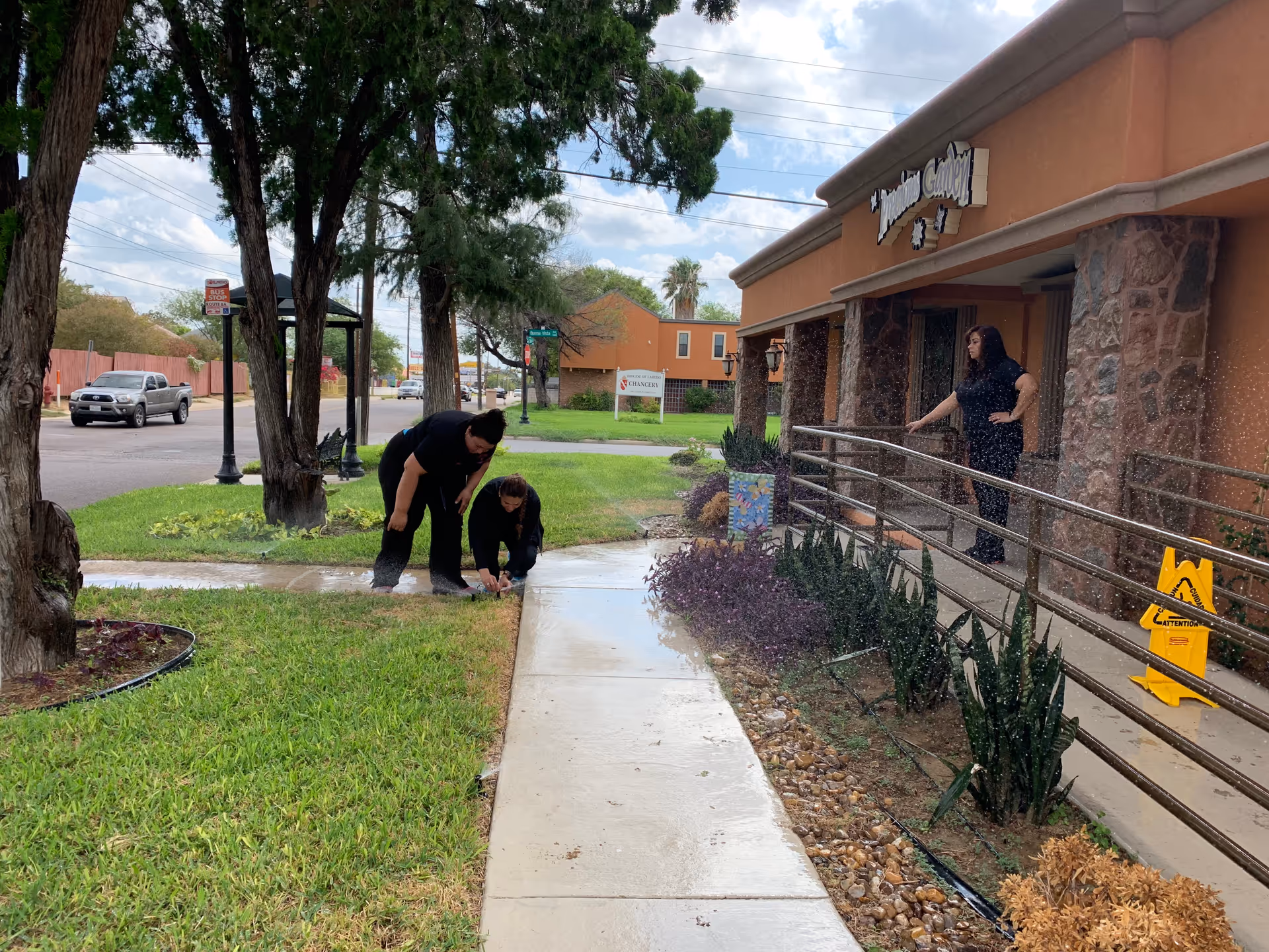 Three people outside Precious Garden Primary Care near the entrance with a ramp.