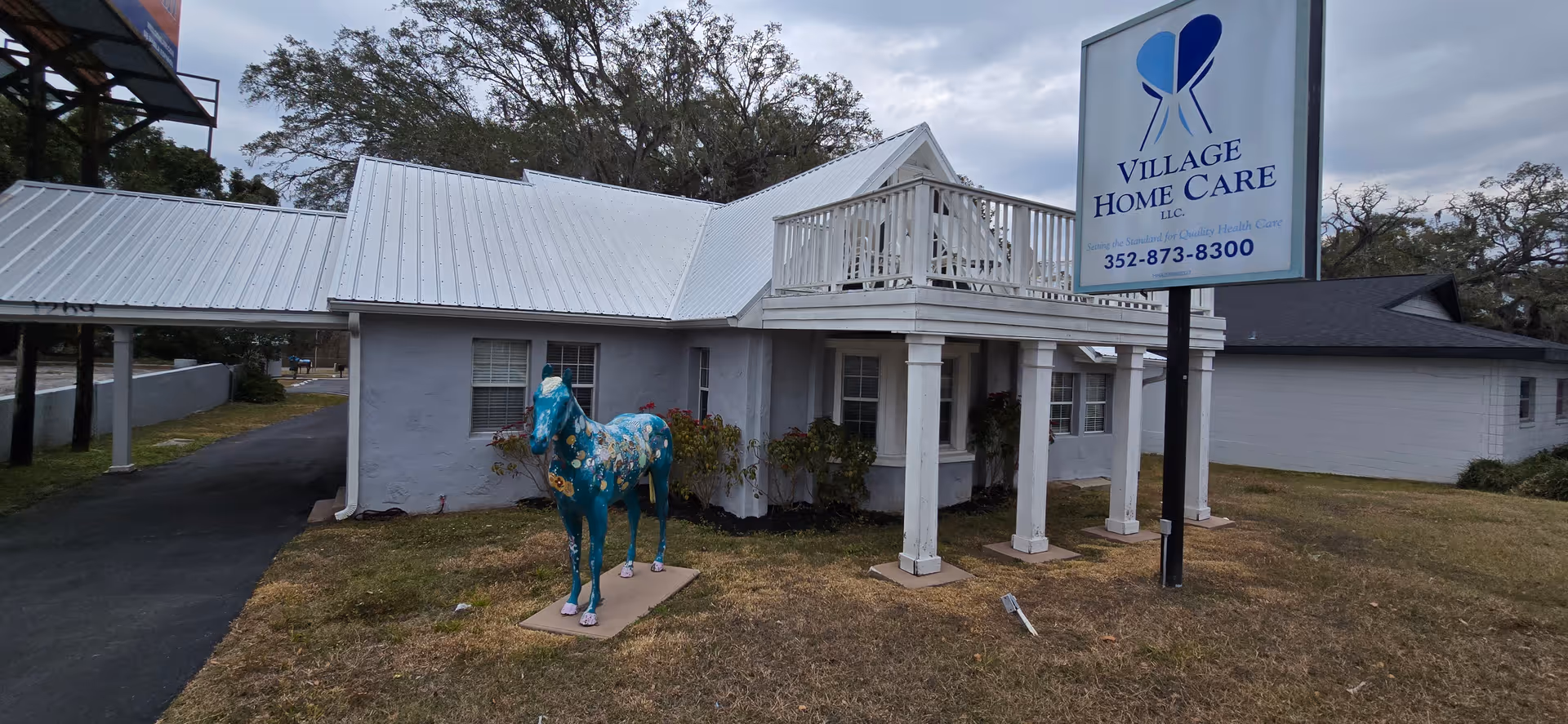 White single-story building with metal roof, Village Home Care sign, and a turquoise horse statue.