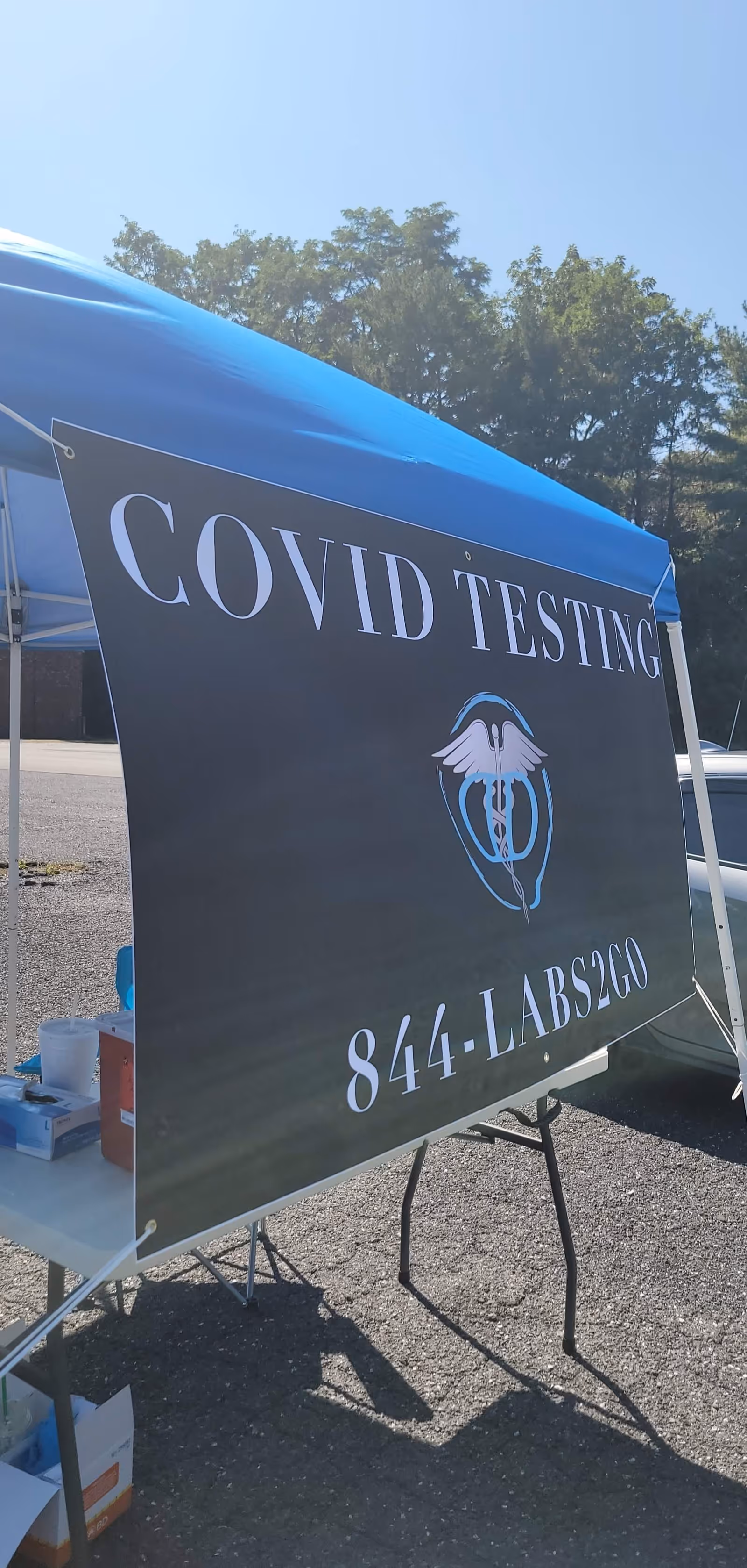 Outdoor COVID testing sign under a blue canopy in a parking lot.