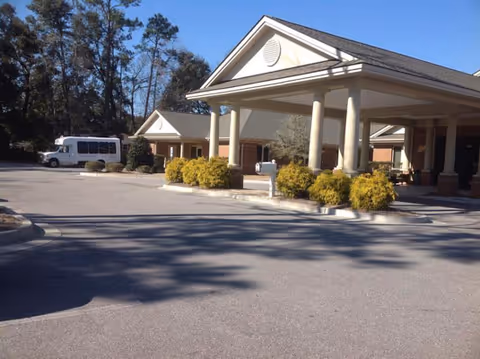 The entrance facade of Anderson Oaks Assisted Living, featuring a covered porch supported by columns, surrounded by landscaped greenery and a parking area.