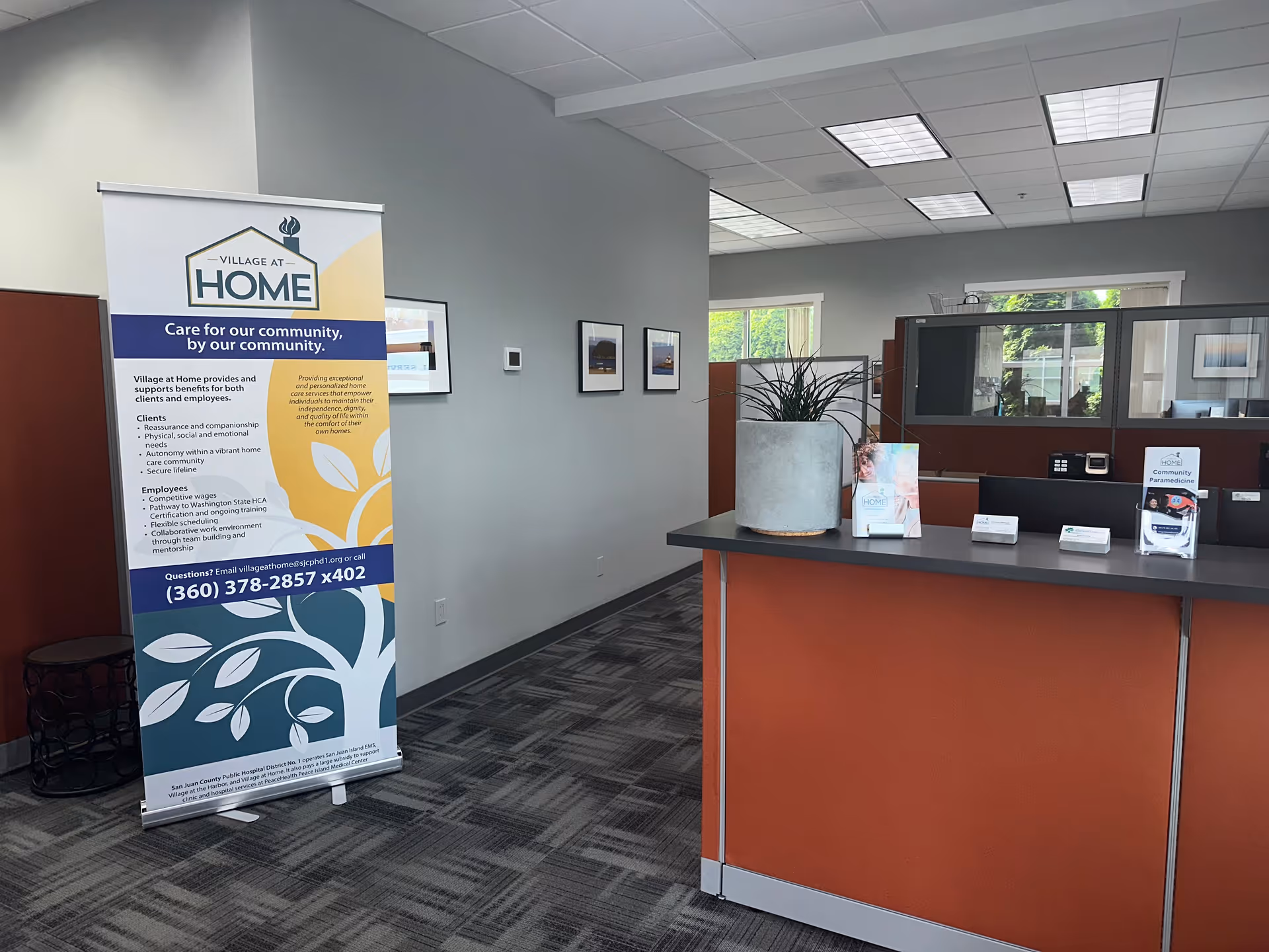 Lobby reception area with a tall banner, orange front desk, and a potted plant.