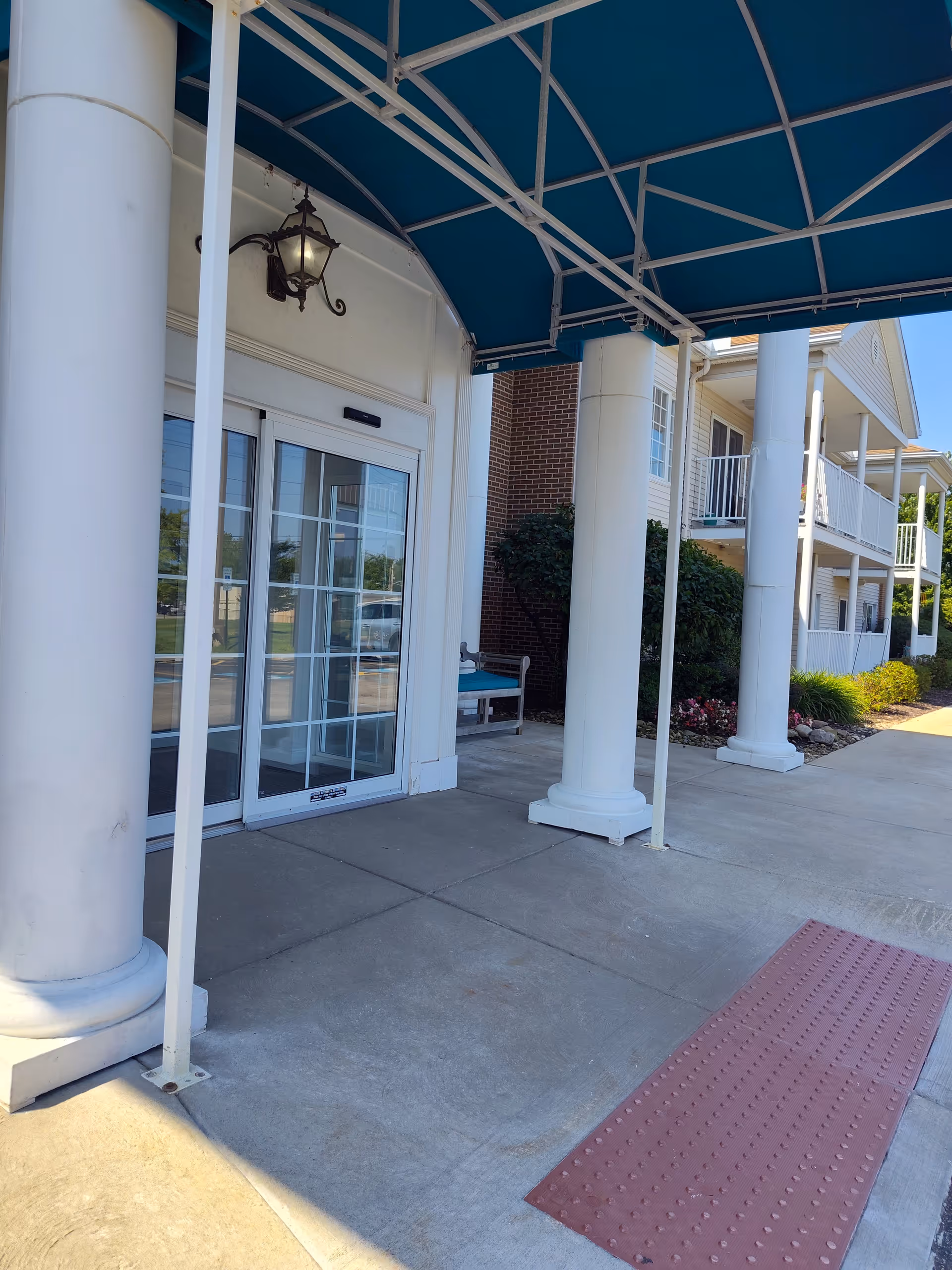 Exterior entrance of Shurmer Place at Altenheim with white columns and glass doors.