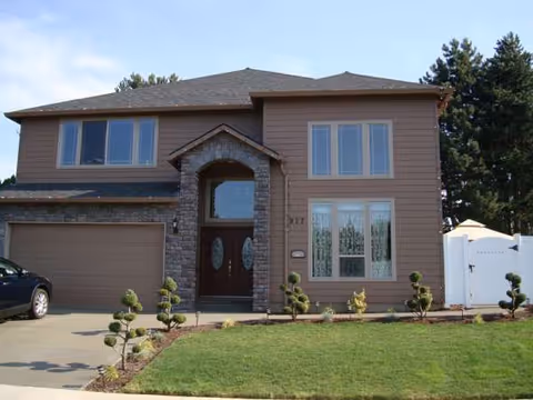 Two-story beige home with stone entryway, attached garage, and a manicured front yard.