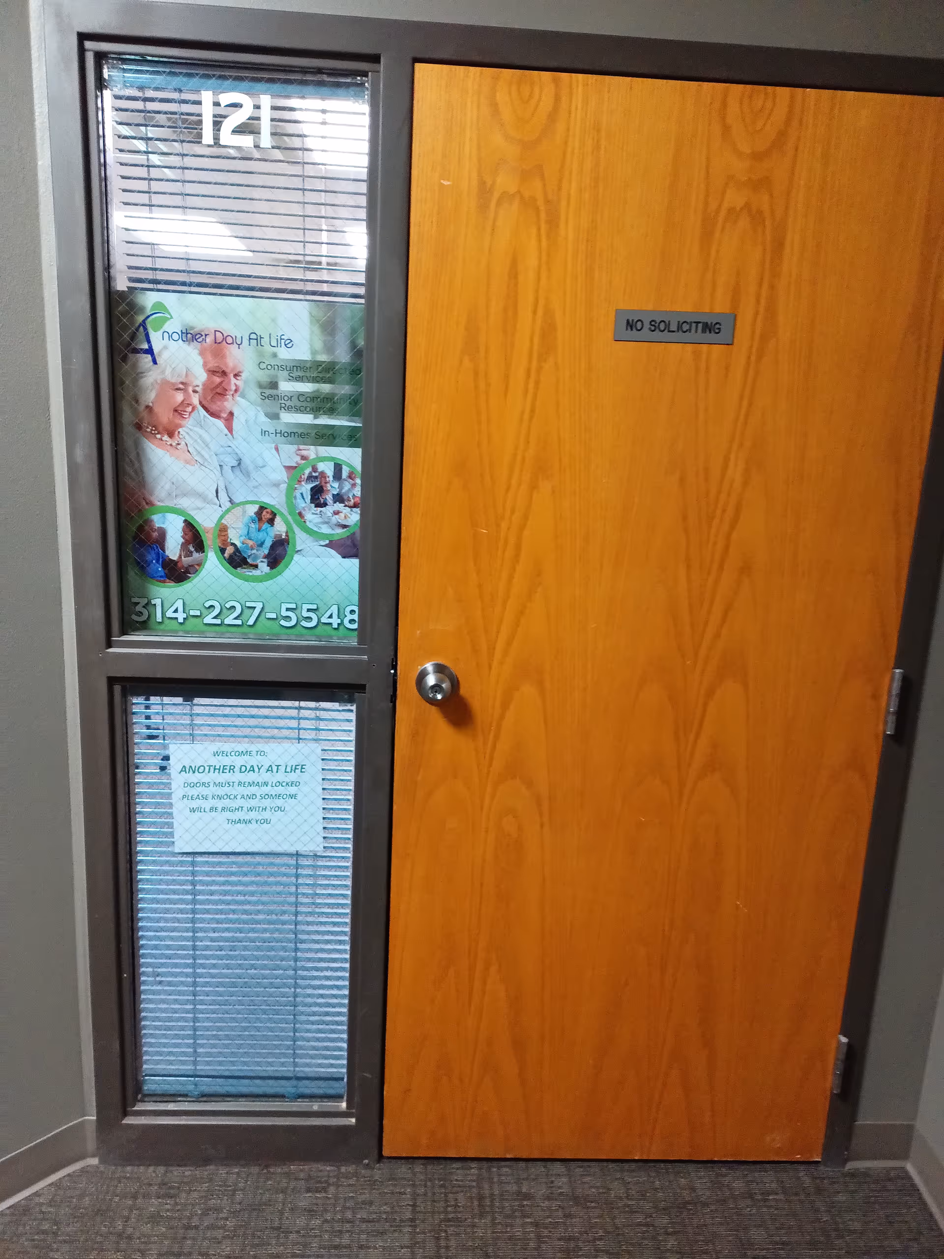 Wooden door with No Soliciting sign beside glass wall displaying posters.