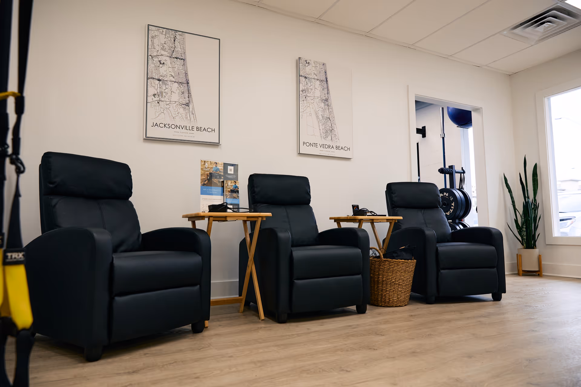 Waiting area with three black recliners, small tables, and maps on the wall.
