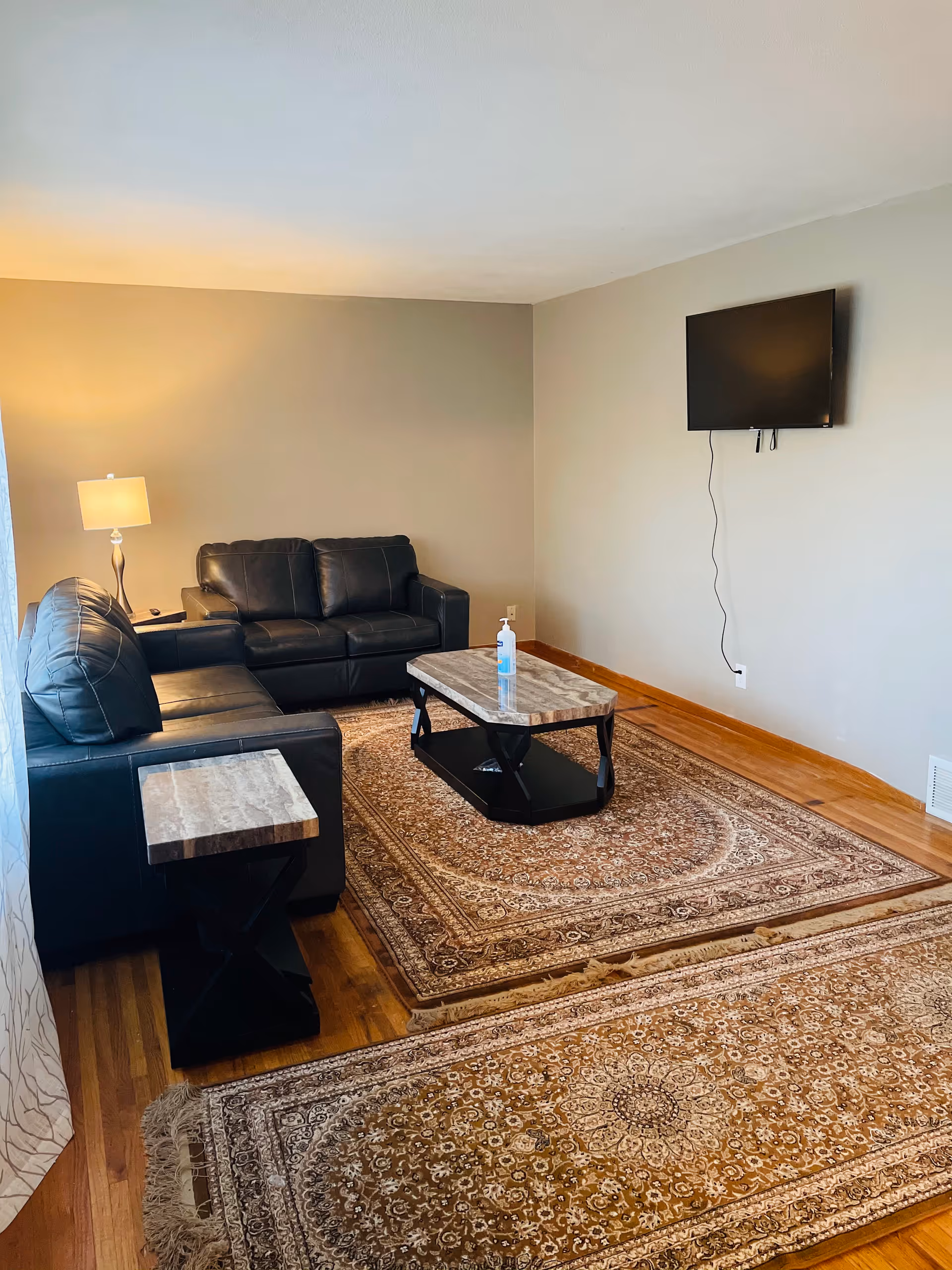 Cozy living room with black leather sofas, a wall-mounted TV, coffee tables, and a rug.
