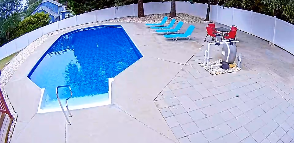 Outdoor pool area with blue lounge chairs, tables, and a pool pump.
