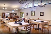 A bright dining room in a senior living facility with tables set under chandeliers.