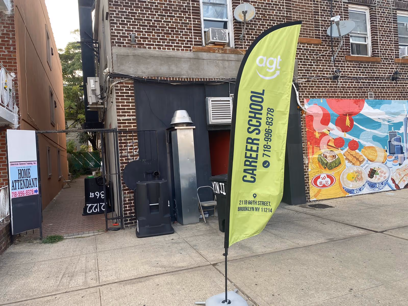 Brick building exterior along sidewalk with neon green Career School banner and mural wall.