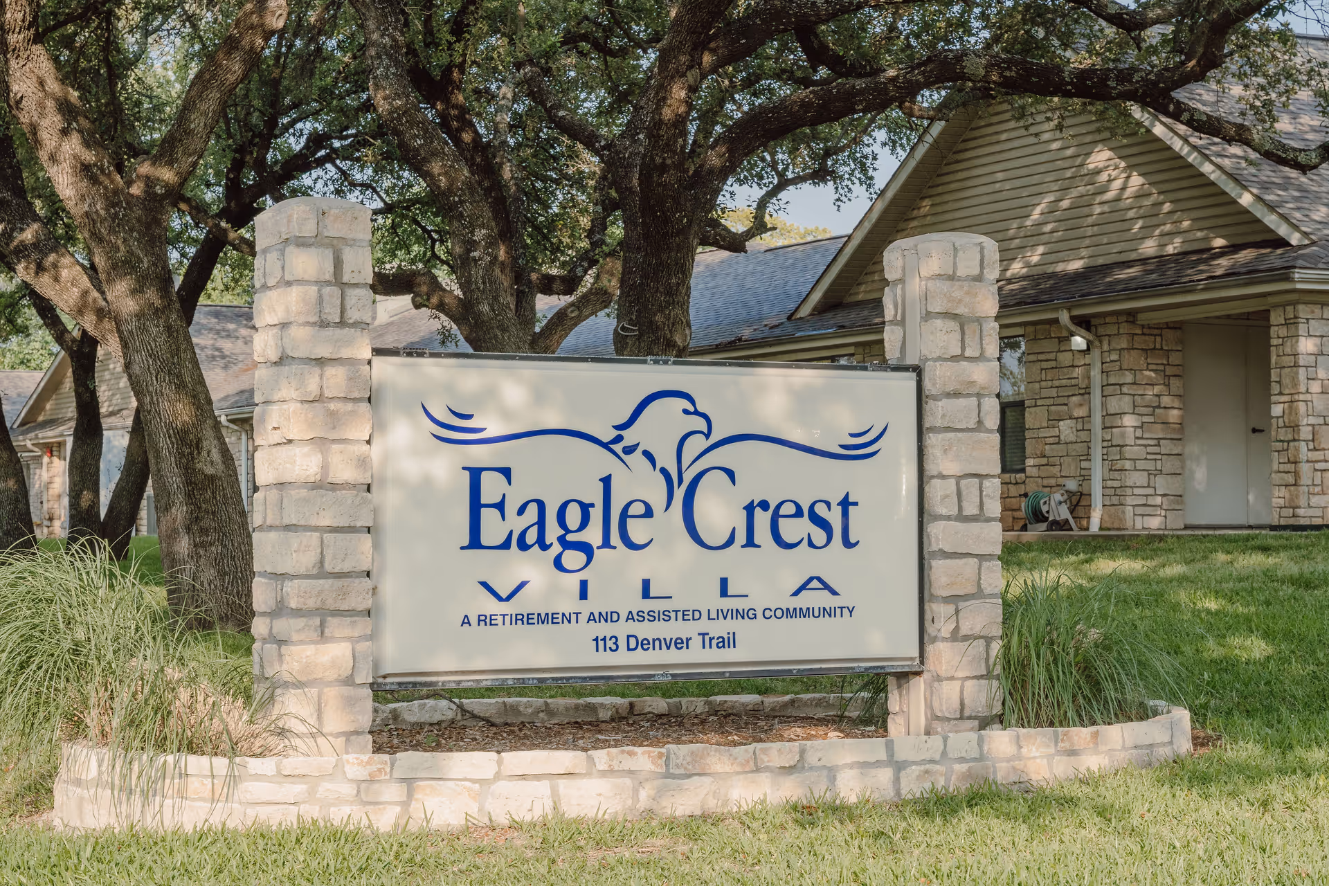 Exterior view of Eagle Crest retirement community sign beside a stone building and trees