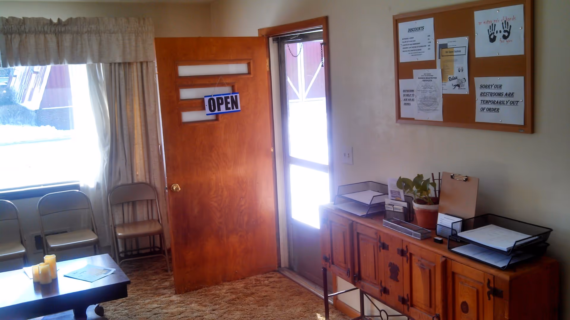 Wooden door labeled OPEN beside bulletin board and cabinet in a small reception area.
