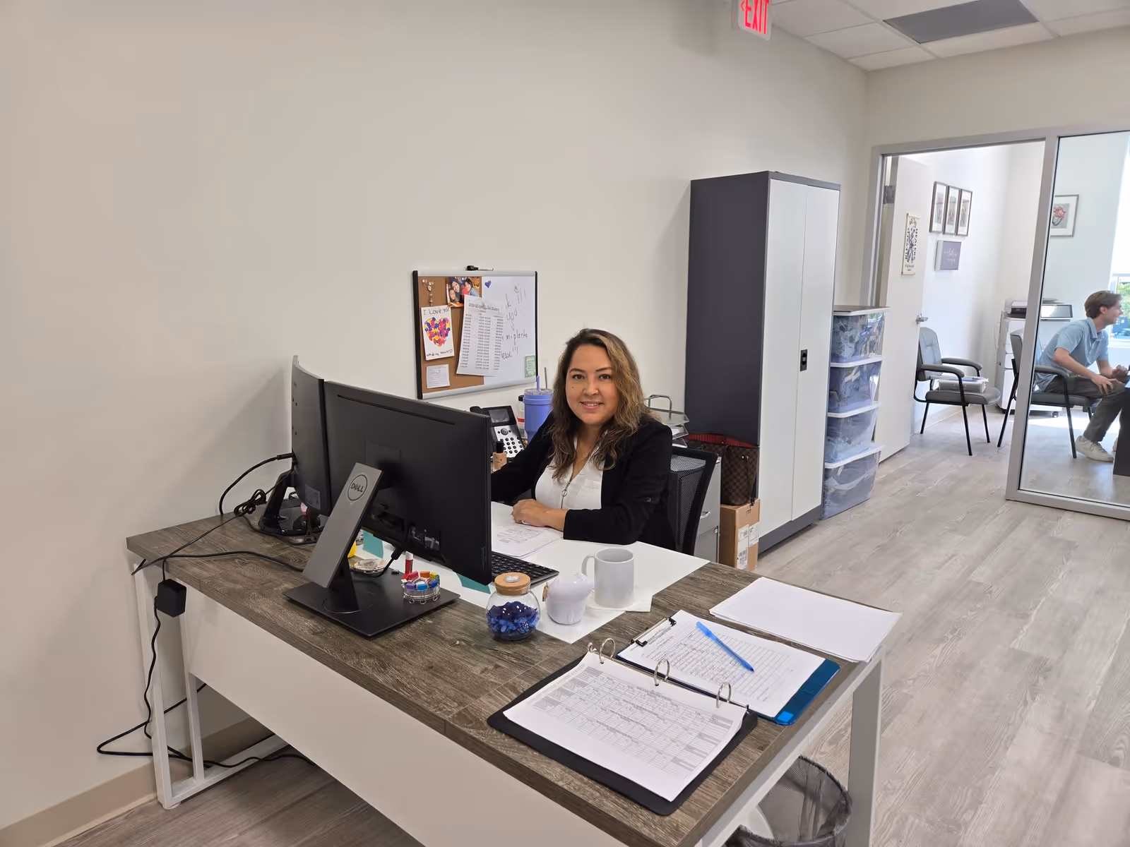 Receptionist sits at desk with computer in an office area of a senior living facility.