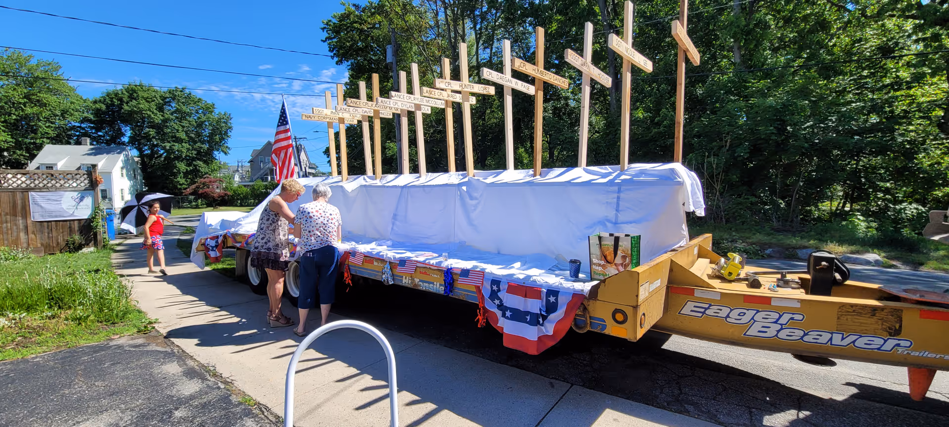 Outdoor parade float on a trailer with crosses and people gathered nearby.