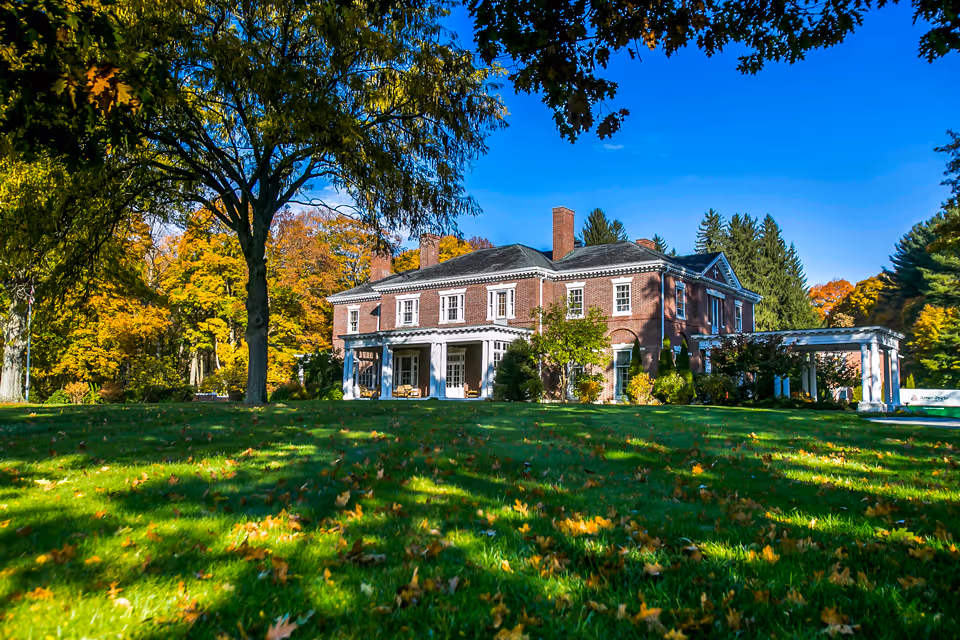Exterior view of the Sugar Hill Assisted Living building with a broad lawn and fall foliage.