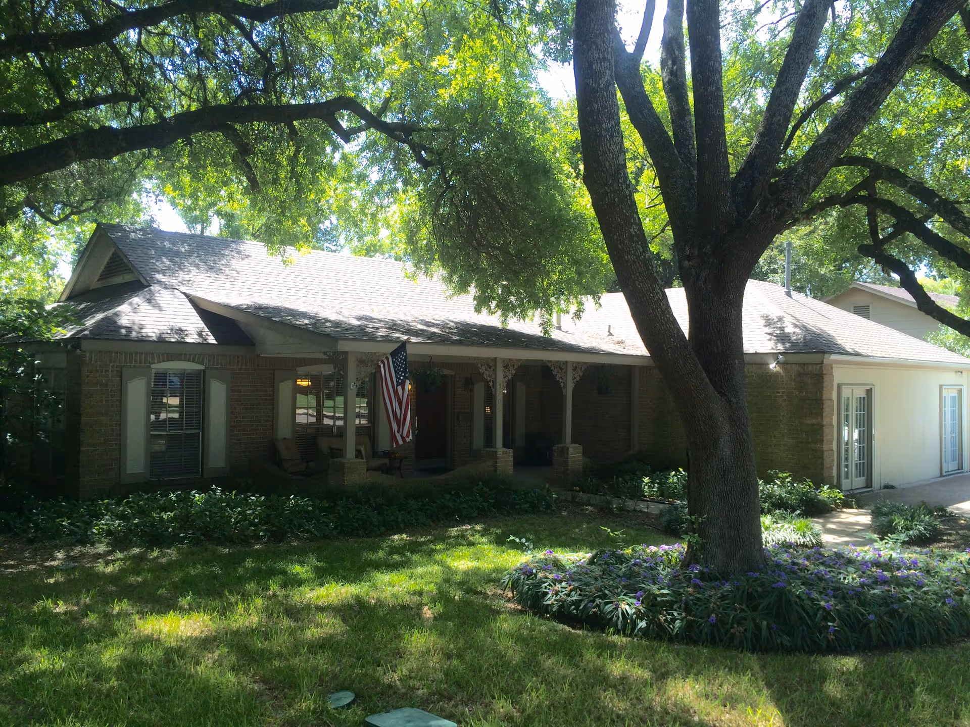 Single story brick facility with a front porch, American flag, and large tree in front yard.
