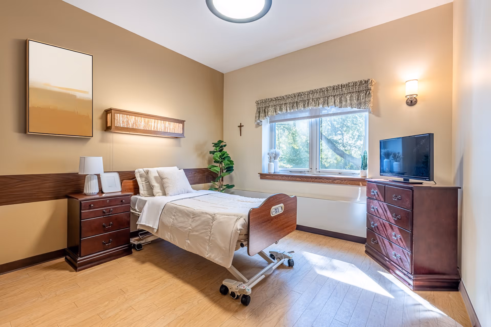 Warmly lit bedroom in a senior facility with an adjustable bed, dresser, and window.