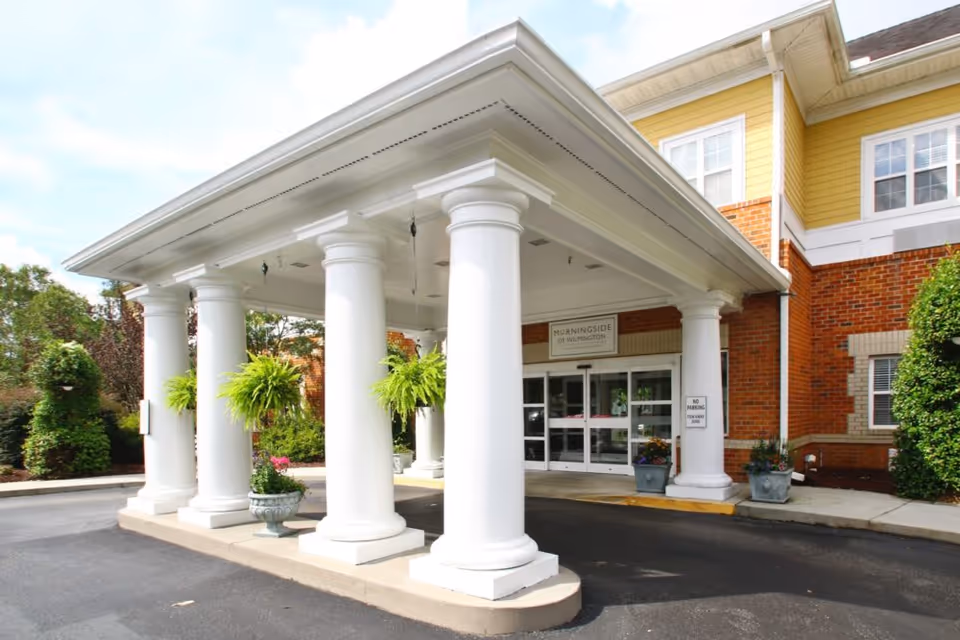 Covered portico with large white columns and potted plants at the front entrance of Morningside of Wilmington.