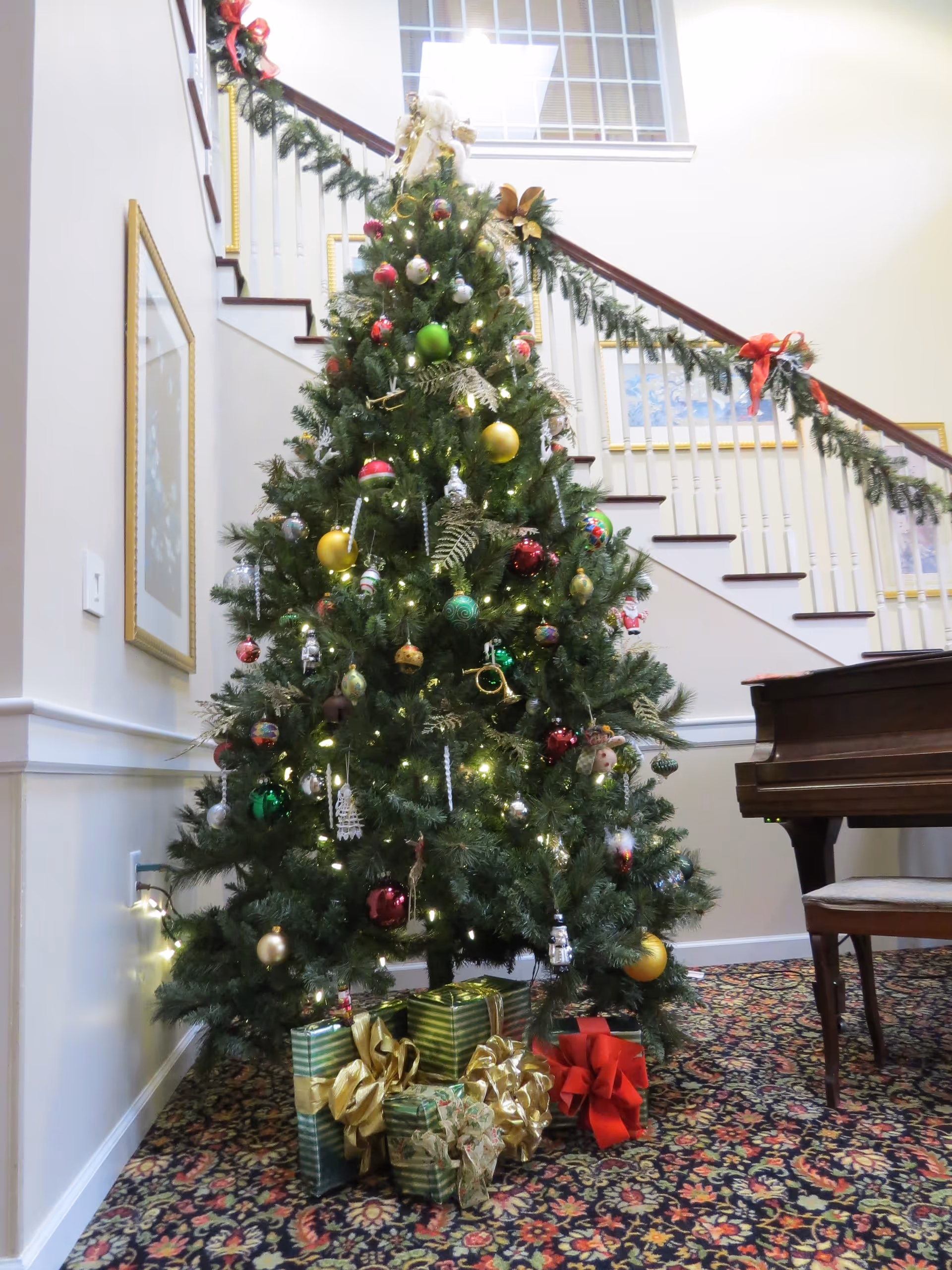 A tall Christmas tree with ornaments and wrapped gifts in a bright interior lobby.
