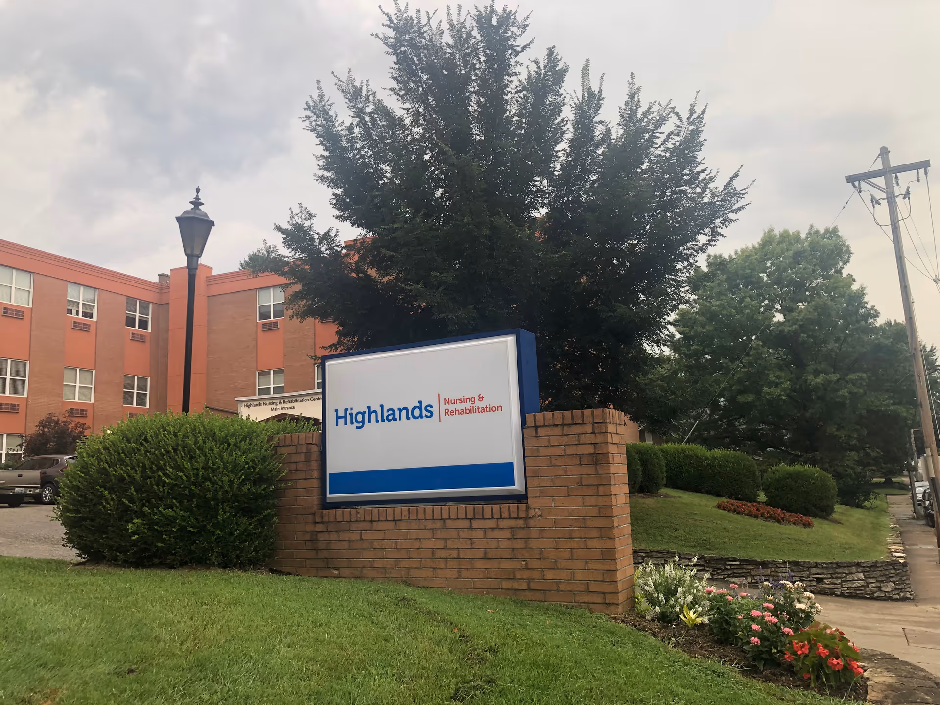 Exterior view of Highlands Health and Rehabilitation Center with a brick sign and landscaping.