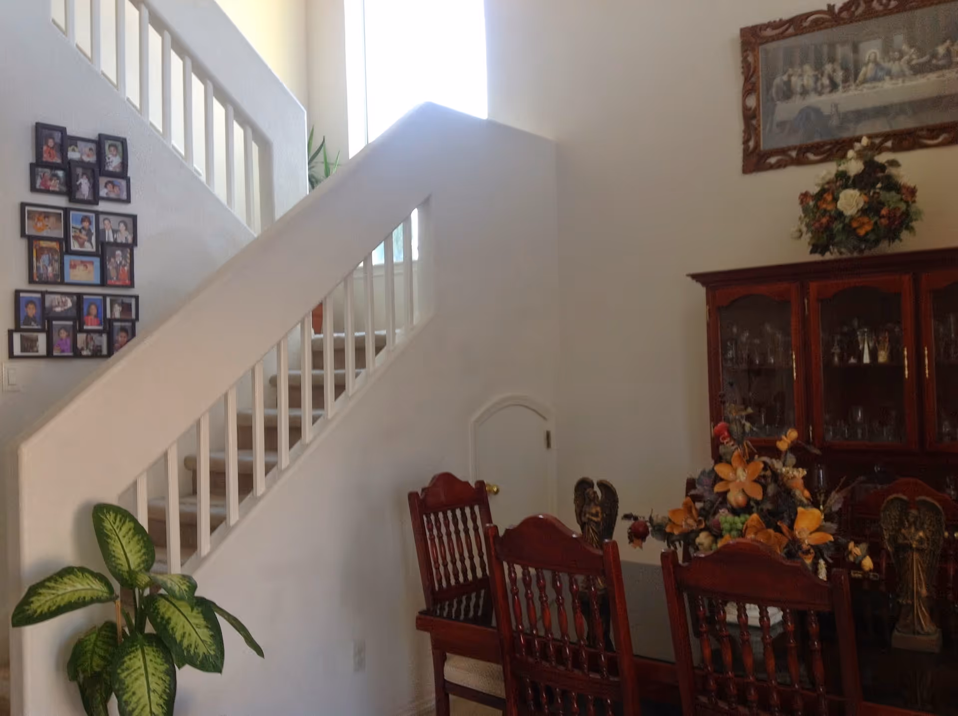 Dining area with wooden chairs, a china cabinet, staircase, and floral centerpiece.