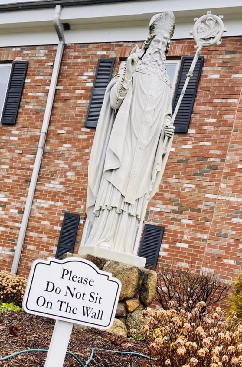 Exterior view at St Patrick's Manor showing a white saint statue near a brick building.