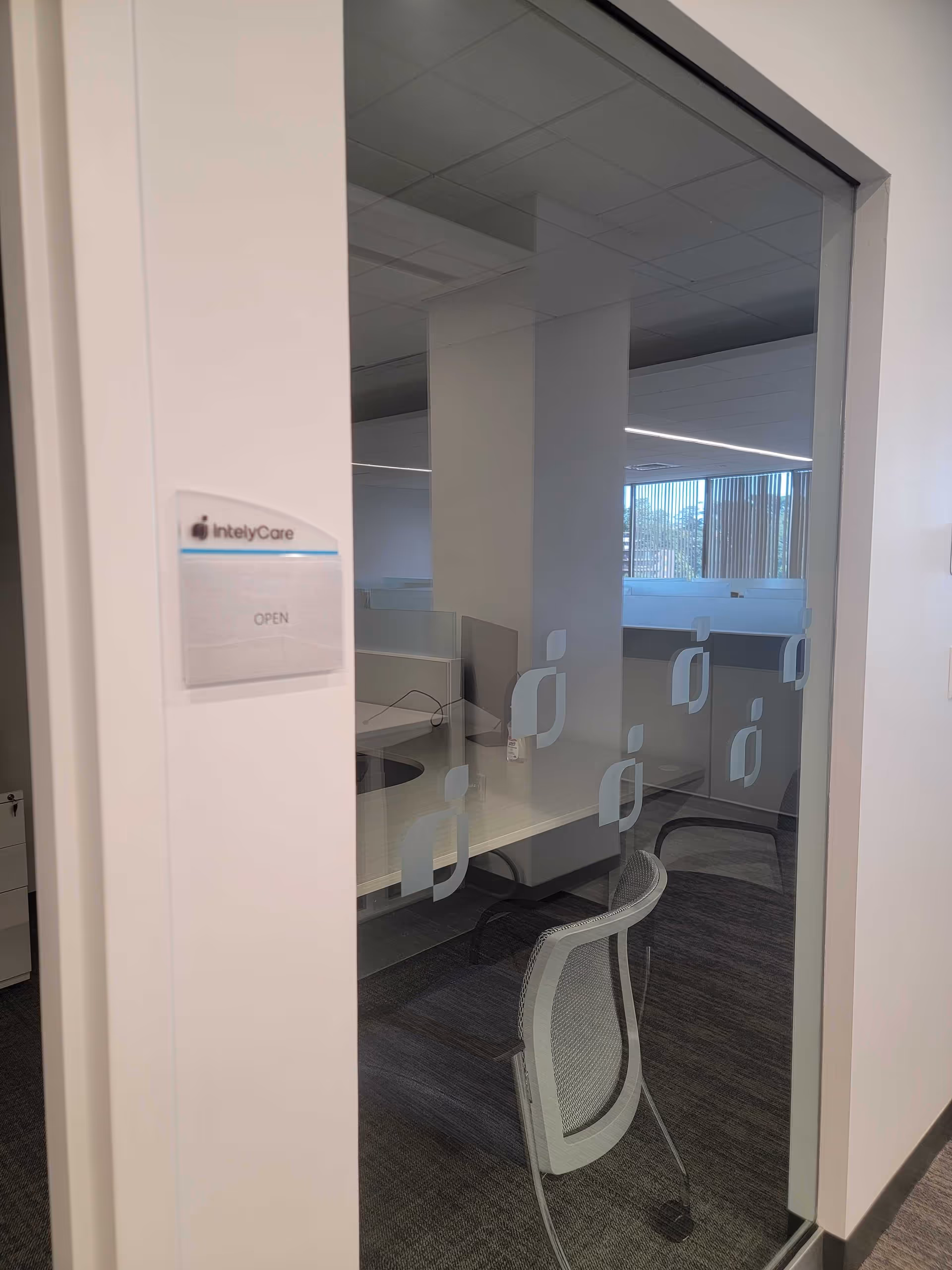Glass-walled office inside a facility with a desk, chair, and IntelyCare OPEN sign.