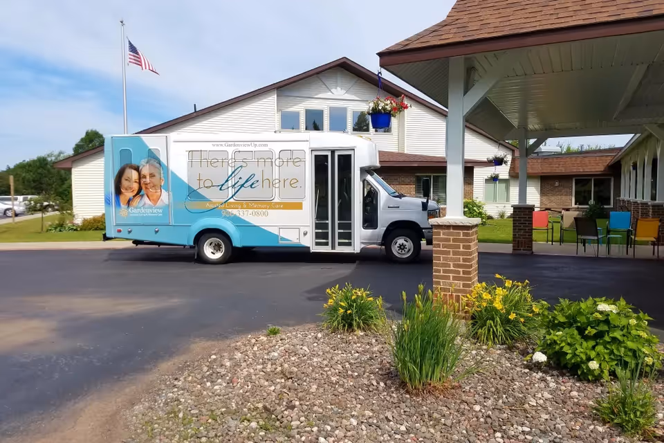 A Gardenview shuttle van parked at the covered entrance of a senior living building with landscaping and outdoor seating.