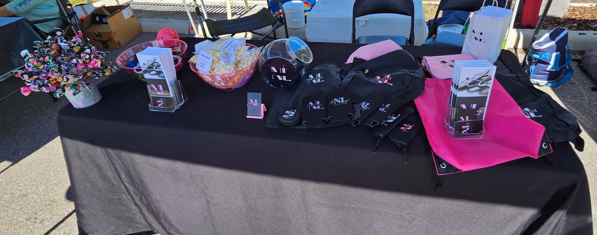 Outdoor table display with Next Level Concierge promotional items, bags, baskets, and brochures.