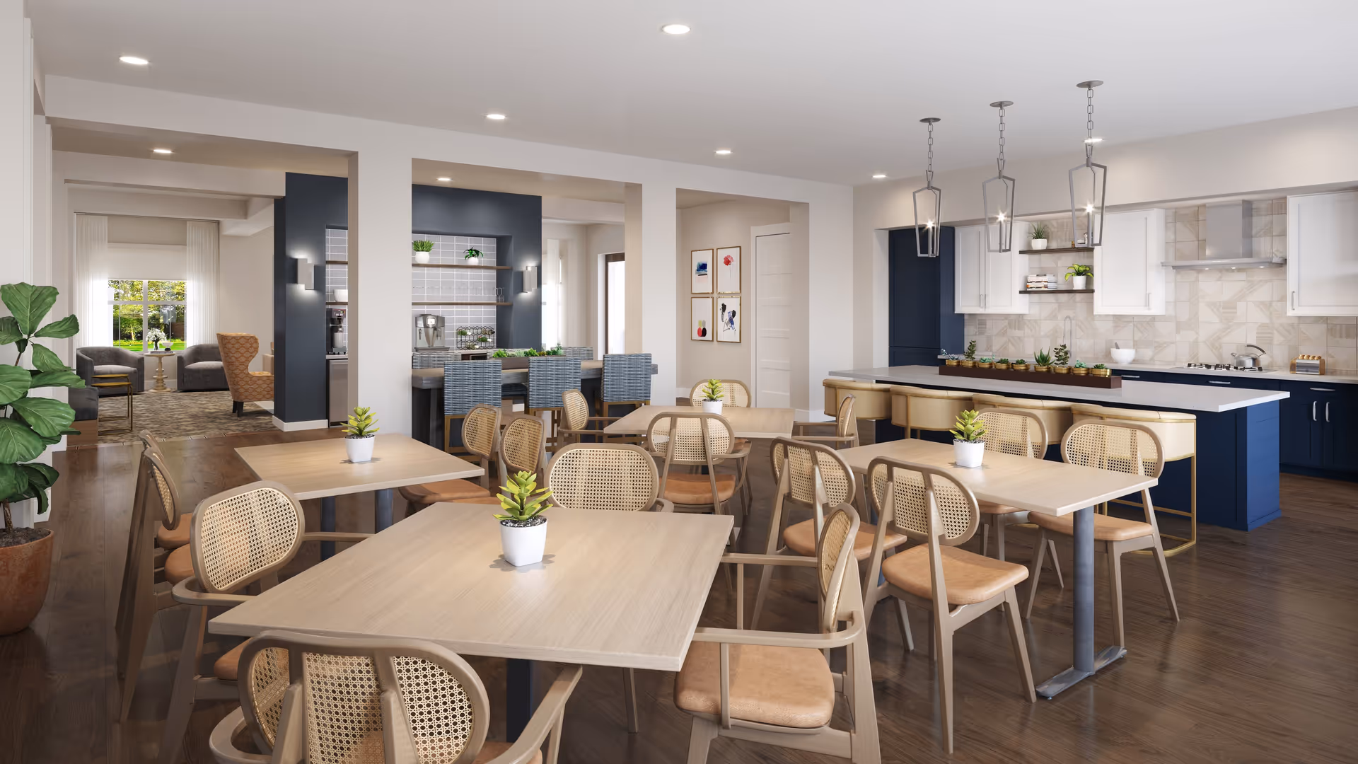 A modern dining area in a senior living facility featuring multiple light wood tables with wicker-backed chairs. Each table has a small potted plant centerpiece. In the background, there is a kitchen with dark blue lower cabinets, white upper cabinets, a tiled backsplash, and a large island with beige bar stools. Pendant lights hang above the island. To the left, there is a cozy seating area with armchairs and a window showing greenery outside.