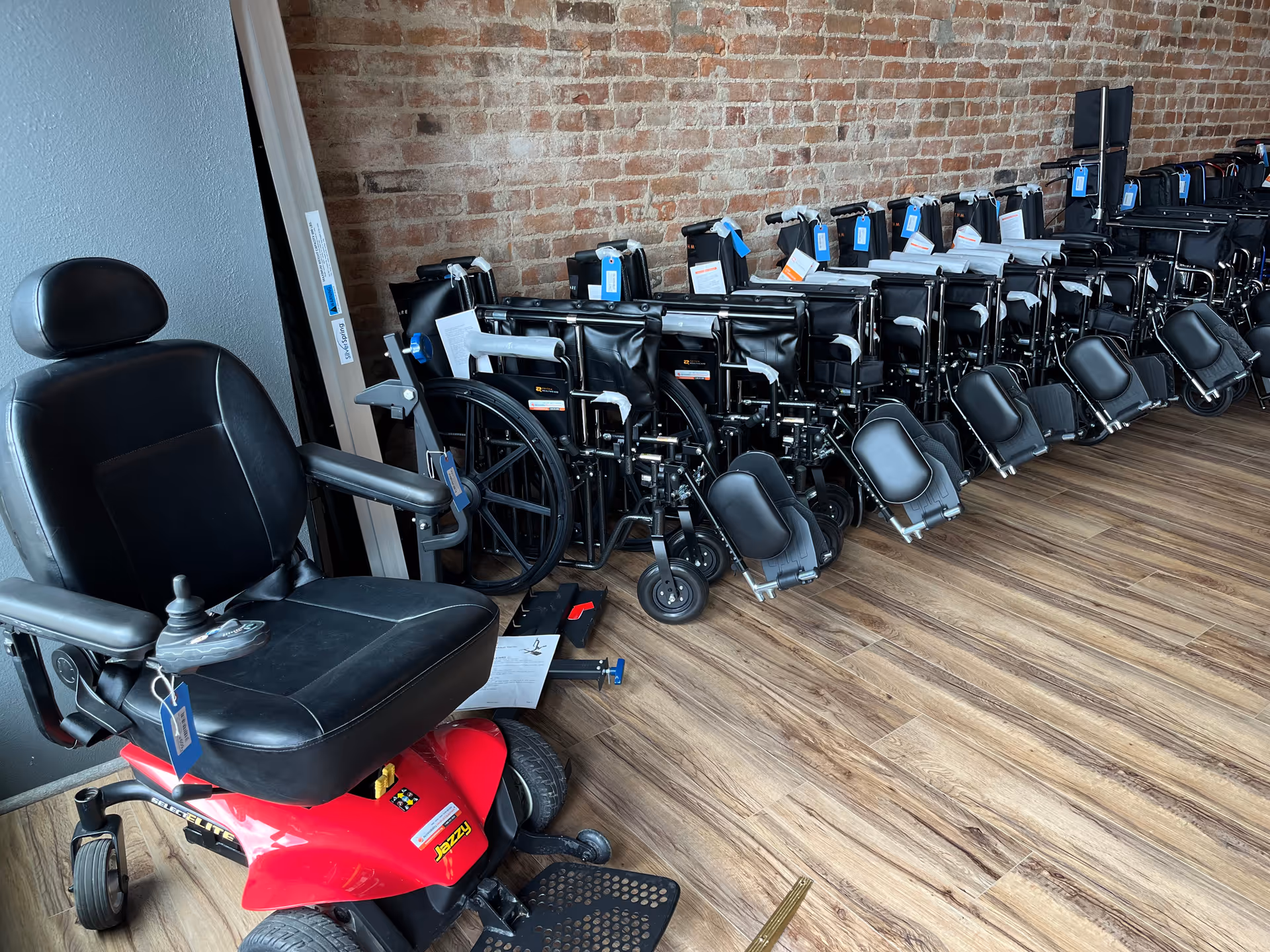 Row of wheelchairs and a mobility scooter lined up along a brick wall storage area.